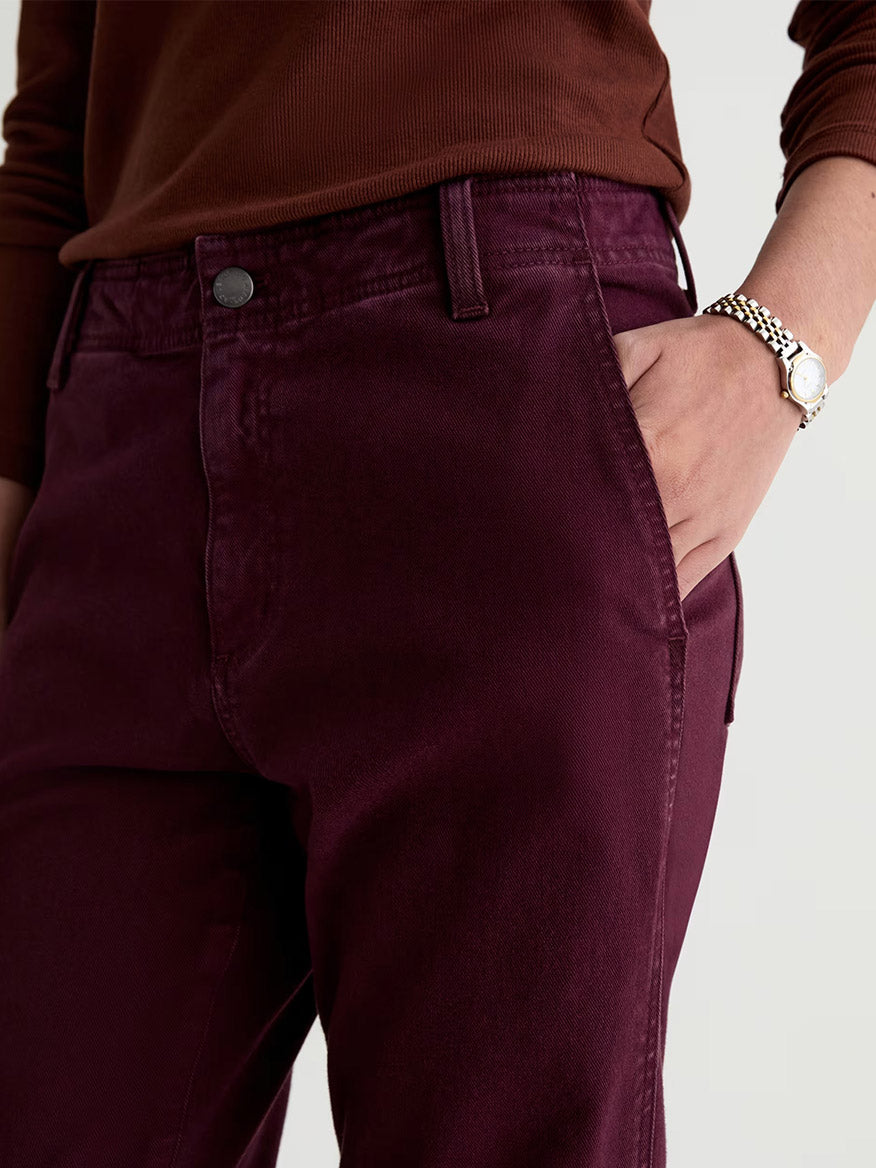 Person wearing AG Jeans Brinley Mid-Rise Straight in Sulfur Jazz Berry and a brown top, with one hand in their pocket and a silver watch on their wrist.