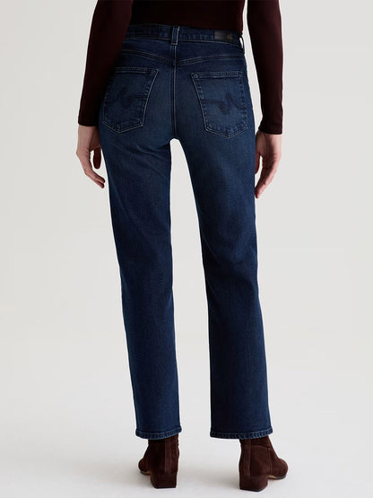 A person wearing AG Jeans Brinley Mid-Rise Straight in Midnight Sun and brown ankle boots, viewed from the back against a plain background.