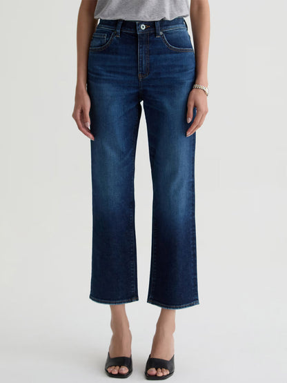 A person wearing a gray top, AG Jeans Brinley Crop in Outspoken, black open-toe sandals, and a bracelet stands against a plain light background.