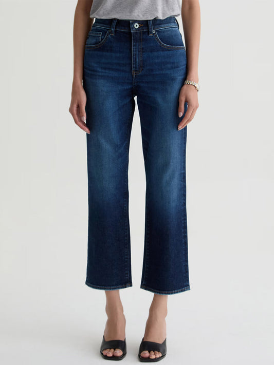 A person wearing a gray top, AG Jeans Brinley Crop in Outspoken, black open-toe sandals, and a bracelet stands against a plain light background.