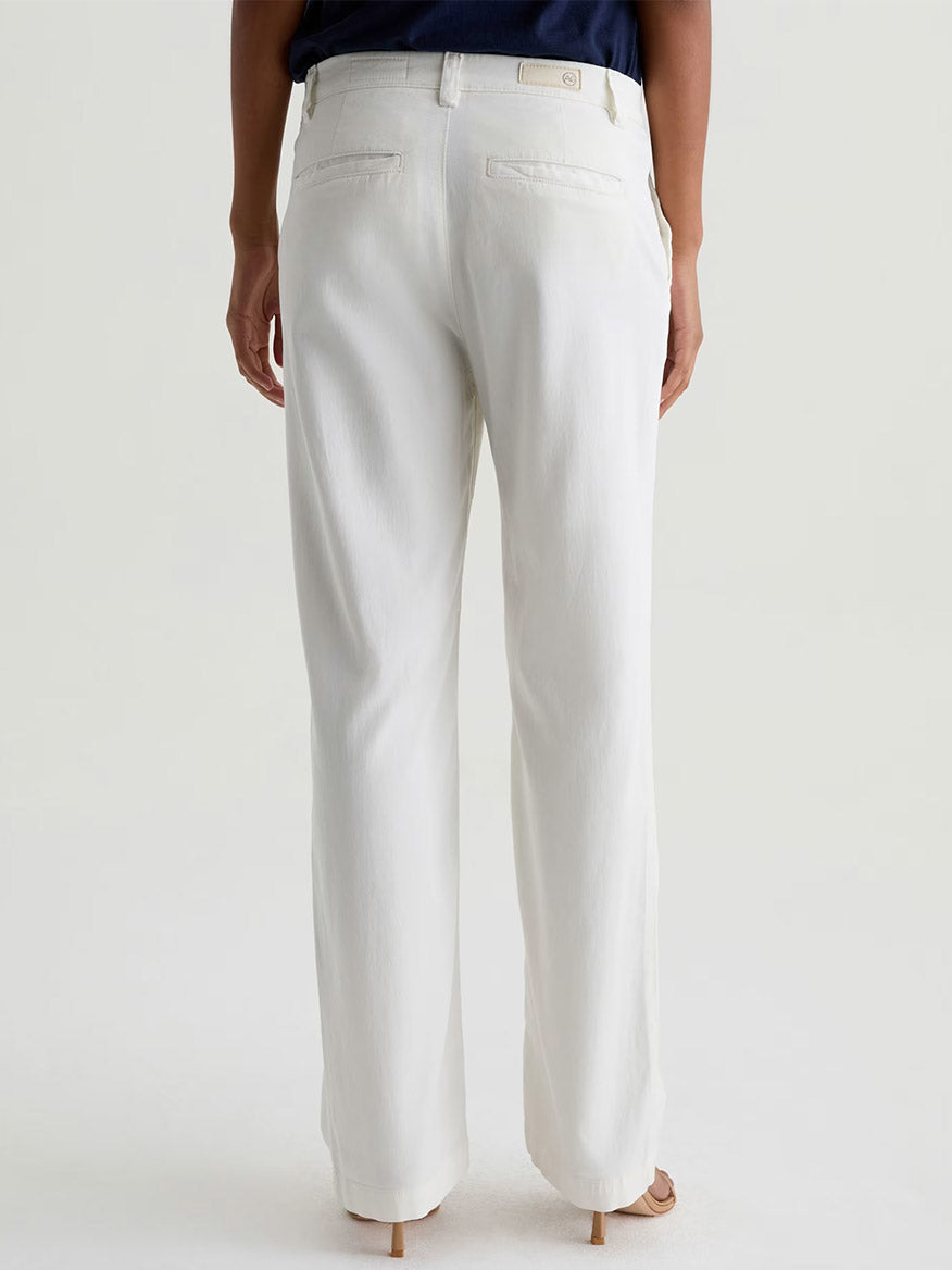 Person wearing AG Jeans Caden Straight Leg Trouser in Powder (white, tailored fit) with a dark top, shown from the back and standing on a light-colored floor.