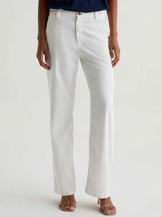 A person in AG Jeans Caden Straight Leg Trouser in Powder, paired with a navy top and open-toed sandals, stands against a plain light background.