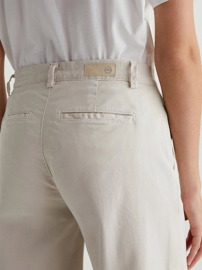 A person stands in a side view, wearing relaxed fit AG Jeans Caden Wide-Leg Trousers in Pumice, paired with a crisp white shirt.