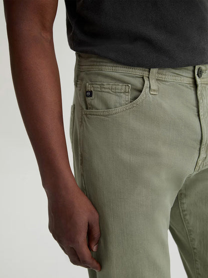 Wearing AG Jeans Everett Linen Slim Straight Pant in Sulfur Spruce Green and a dark shirt, the person is shown from mid-torso to mid-thigh with their left arm relaxed by their side.
