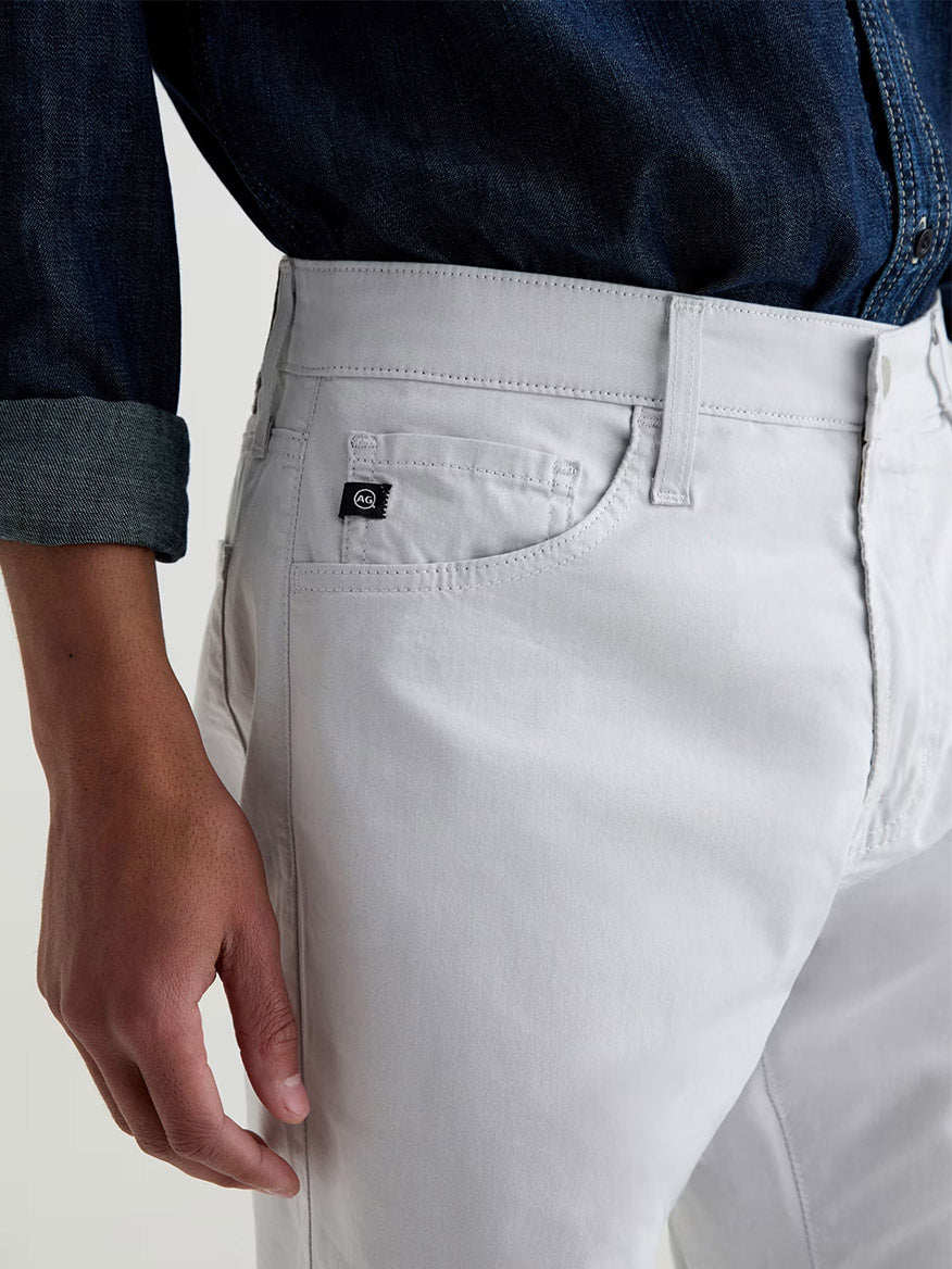 Someone wearing the AG Jeans Everett Airluxe™ Slim Straight Pant in Almost White and a dark denim shirt with rolled cuffs, featuring a close-up of the pants pocket and side.