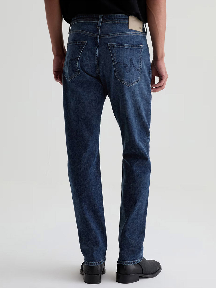Rear view of a person wearing AG Jeans Everett in Sequel slim straight jeans in a medium blue wash and black shoes.