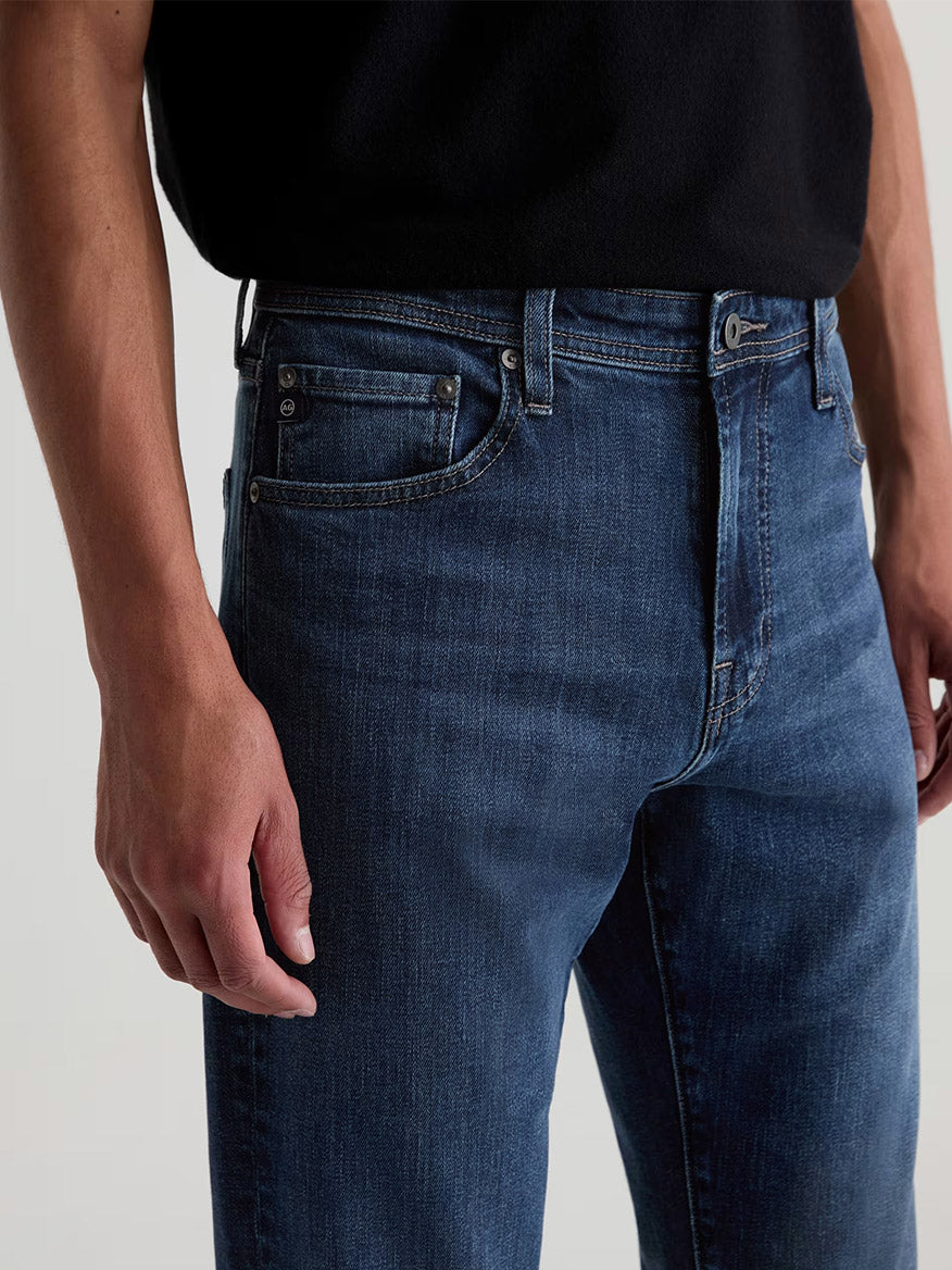 A person wearing AG Jeans Everett in Sequel slim straight jeans in a medium blue wash with a black t-shirt.
