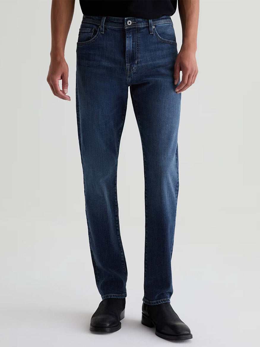 A person wearing AG Jeans Everett in Sequel slim straight jeans in a medium blue wash and black boots.