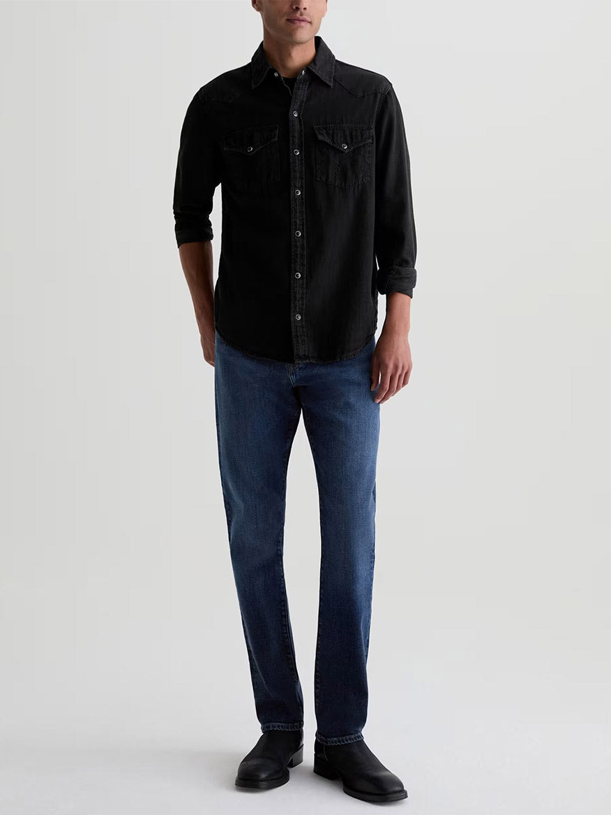 A person wearing a black long-sleeve button-down shirt, AG Jeans Everett in Sequel, and black boots.