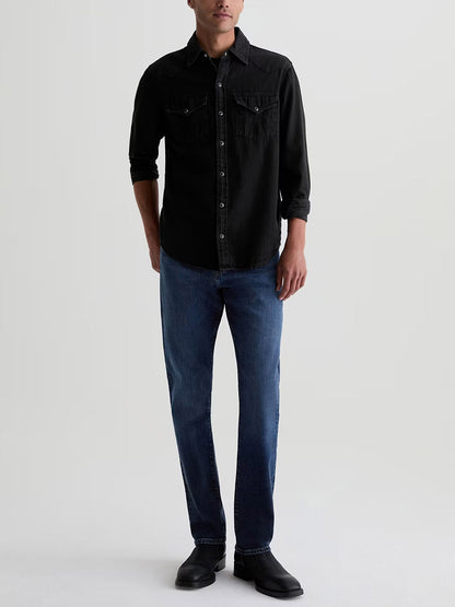 A person wearing a black long-sleeve button-down shirt, AG Jeans Everett in Sequel, and black boots.
