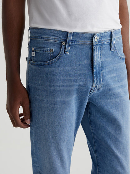 Close-up of a person wearing AG Jeans Everett in Olympus jeans, focusing on the upper part of the slim straight jeans with a hand resting on the hip.