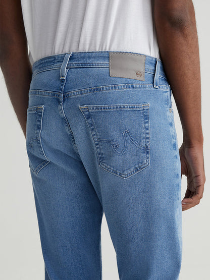 Close-up of the back pocket and waistband of AG Jeans Everett in Olympus slim straight jeans worn by a person, featuring detailed stitching and a leather brand patch.