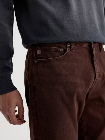 A person wearing a dark gray sweatshirt and AG Jeans Everett in 7 Years Sulfur Wood Brown, shown from mid-torso to thigh with focus on the pocket area.