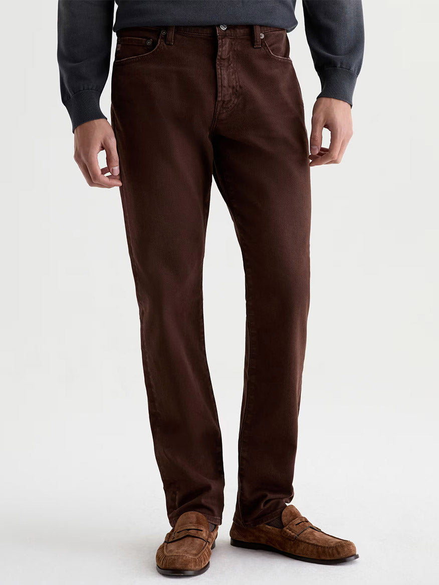 Wearing AG Jeans Everett in 7 Years Sulfur Wood Brown, styled with a dark long-sleeve shirt and brown loafers, a person stands against a plain light background.