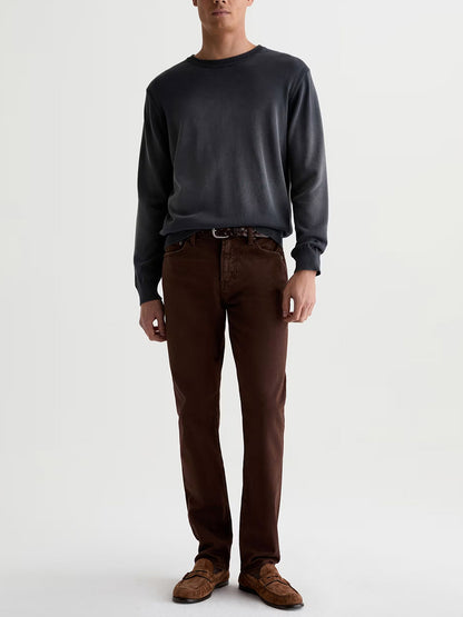 A man stands against a plain white background wearing a dark gray long-sleeve shirt, brown shoes, and AG Jeans Everett in 7 Years Sulfur Wood Brown. His face is not visible.