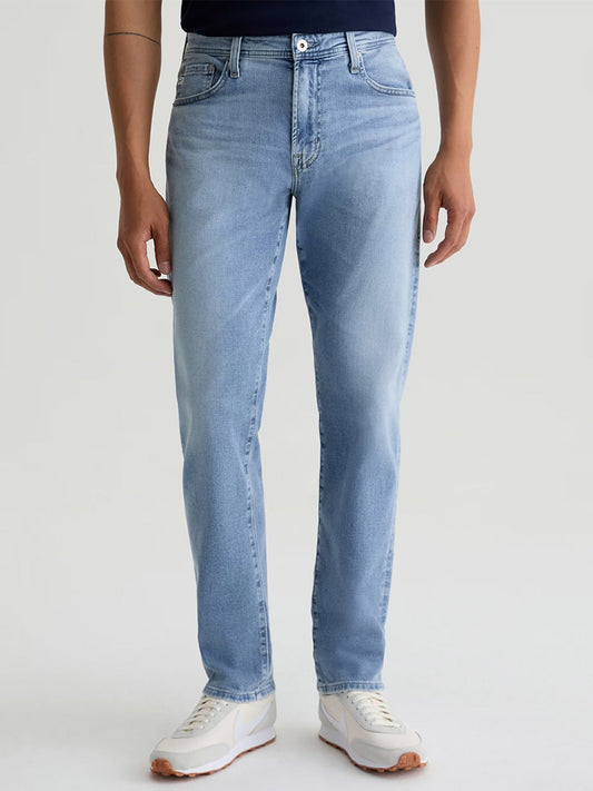 A person in AG Jeans Everett in Saltillo (light indigo wash) and white sneakers stands against a plain light background.