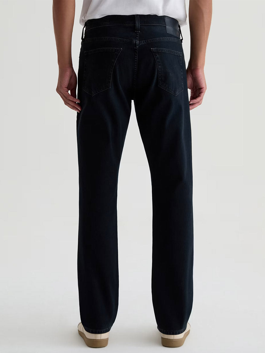 Person standing facing away, wearing AG Jeans Everett 360° Jean in Vintage Ink, a white shirt tucked in, and white sneakers against a plain background.