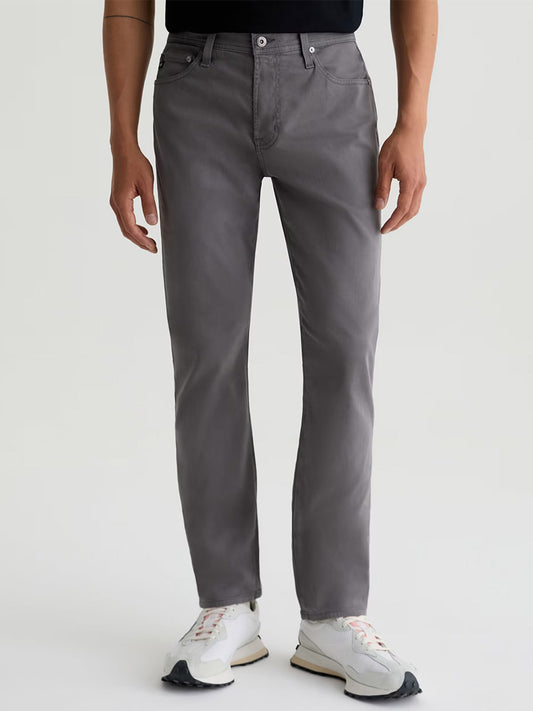 Someone wearing AG Jeans Everett Sueded in Folkestone Grey, a black shirt, and white sneakers stands against a plain light background.