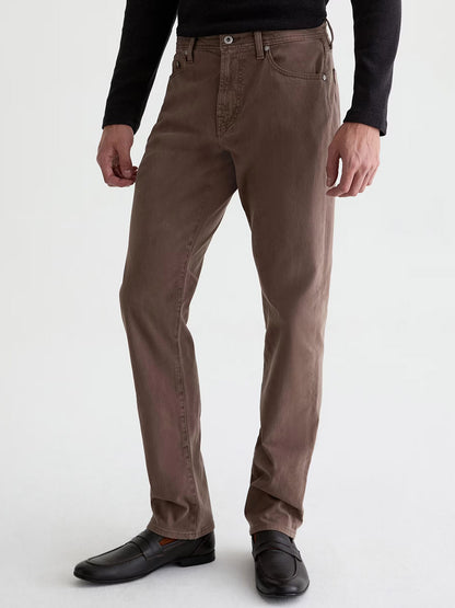 A man wears the AG Jeans Everett Sueded in Sulfur Taupe Grey, paired with a black long-sleeve shirt and black dress shoes, standing against a plain light background for a subtle vintage look.