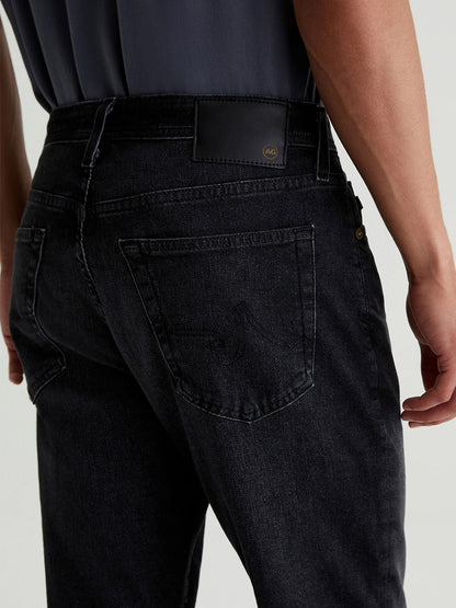 Close-up of a person wearing AG Jeans Everett in Trophy from the back, highlighting the pocket and waistband with a black label, crafted in Hypersoft Black Denim.