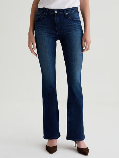 Model wears AG Jeans Farrah Mid-Rise Boot in Epilogue, a dark blue stretch denim, paired with a white top. Only the lower half of her body is visible against a plain light background.