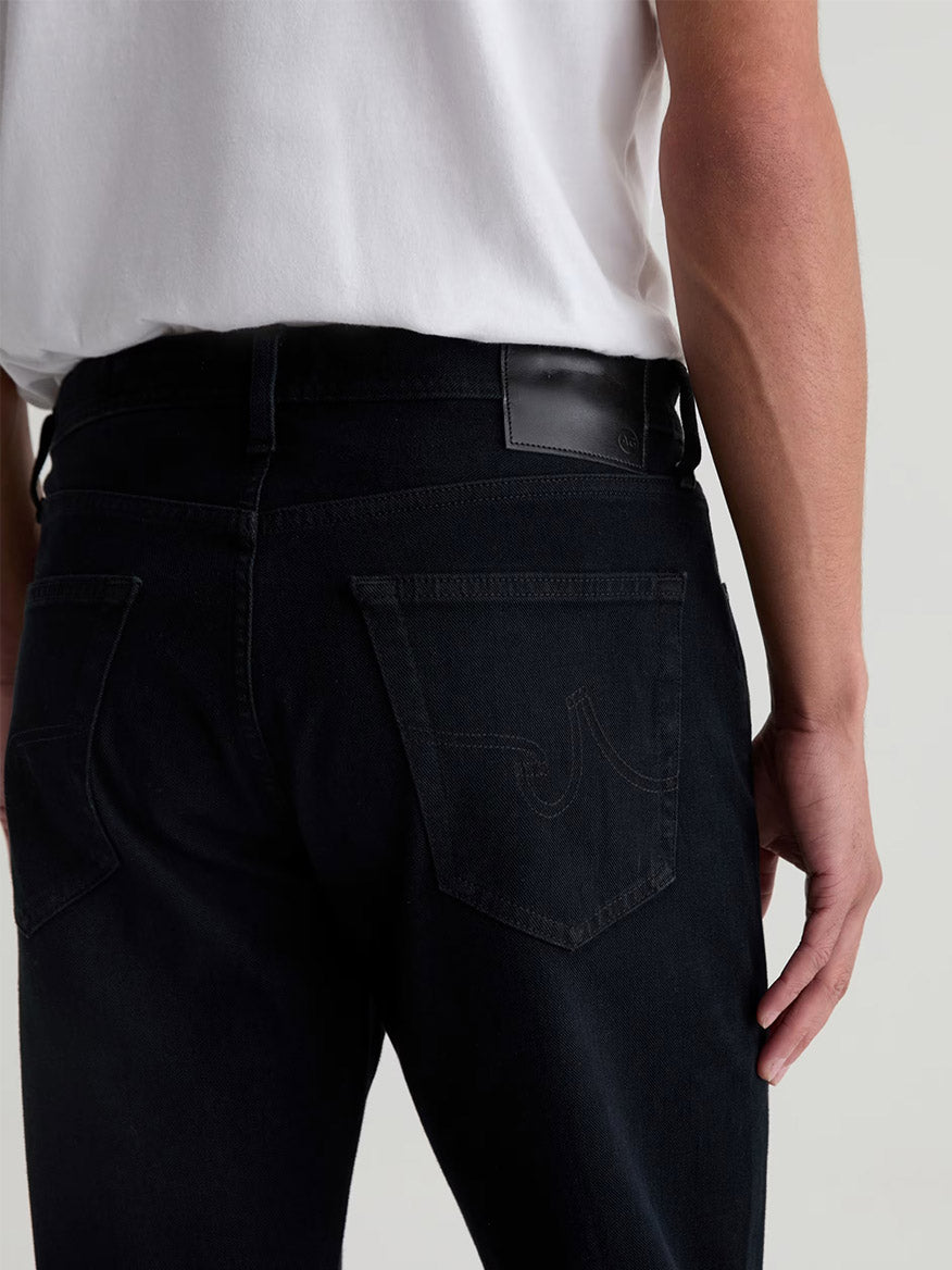 A person wears AG Jeans Graduate in Vintage Ink, shown from the back with focus on the tailored leg’s rear pocket and waistband.