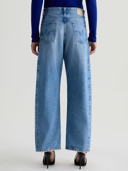 Person wearing AG Jeans Hattie High Rise Barrel in Blueprint, styled with black high heels, photographed from the back against a plain background.