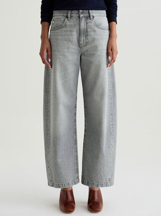 Wearing AG Jeans Hattie High Rise Barrel in Al Fresco—petite-friendly, light gray, high-waisted wide-leg non-stretch denim—with brown heeled shoes, standing against a plain background.