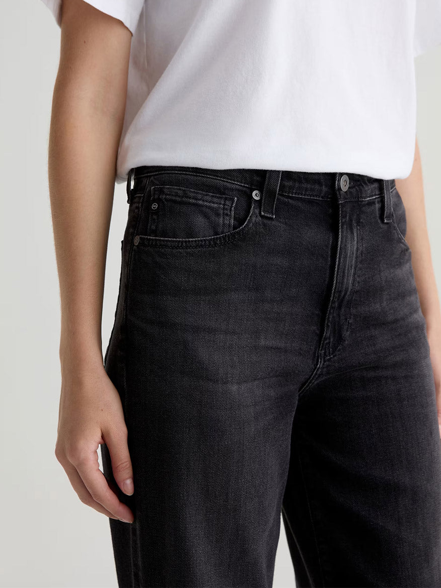 Person wearing a white t-shirt and the AG Jeans Kora High-Rise Wide Leg in Nebula, shown from shoulder to upper thigh with one arm relaxed by their side.
