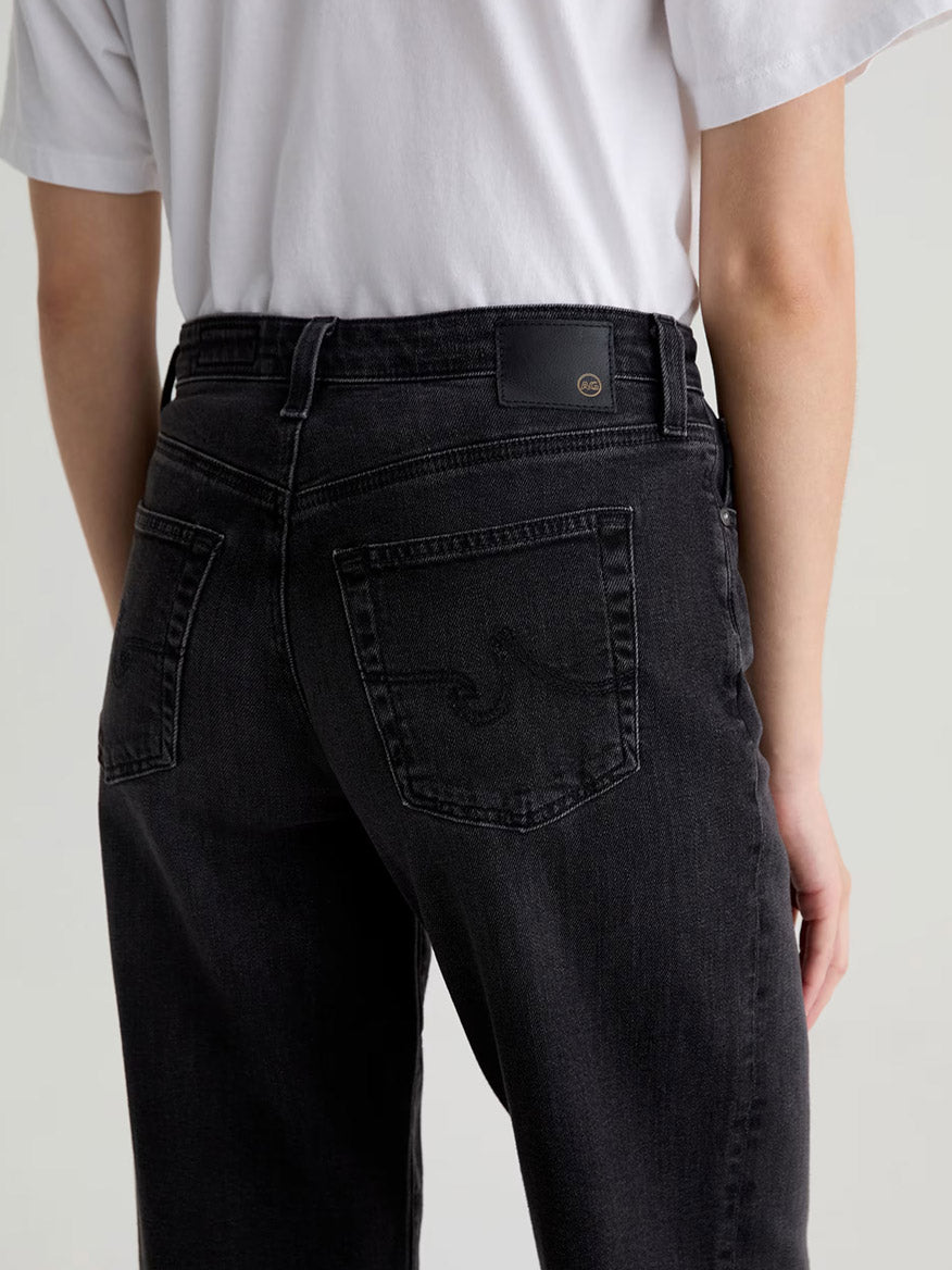 Model shown from the back wearing AG Jeans Kora High-Rise Wide Leg in Nebula, a comfort-stretch black denim with focus on the rear pockets, paired with a white t-shirt.