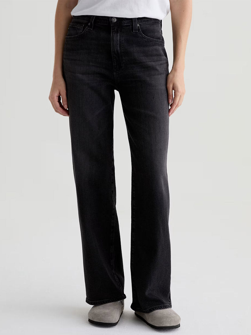 A person wearing a white t-shirt, AG Jeans Kora High-Rise Wide Leg in Nebula, and light gray shoes stands facing forward against a plain background.