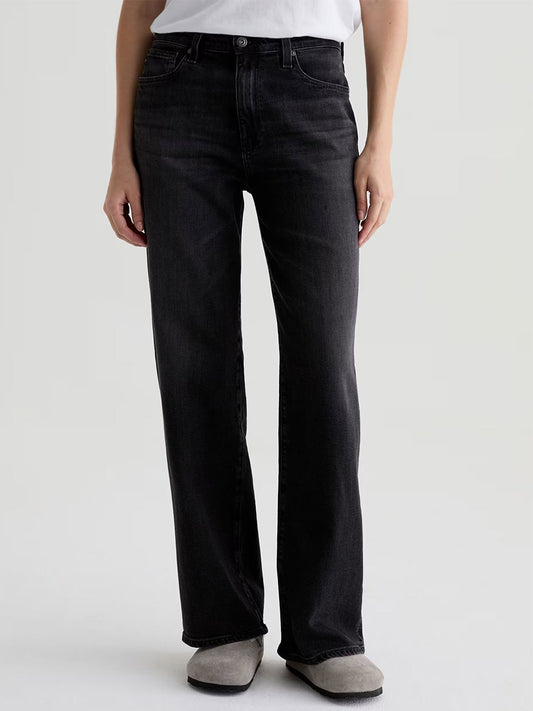 A person wearing a white t-shirt, AG Jeans Kora High-Rise Wide Leg in Nebula, and light gray shoes stands facing forward against a plain background.
