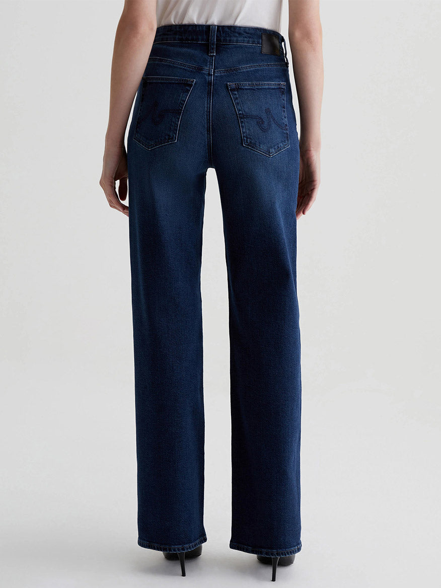 A person is seen from the back wearing AG Jeans Kora High-Rise Wide Leg in Midnight Sun, crafted from vintage comfort stretch denim, and paired with a white shirt.