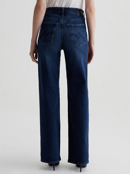 A person is seen from the back wearing AG Jeans Kora High-Rise Wide Leg in Midnight Sun, crafted from vintage comfort stretch denim, and paired with a white shirt.