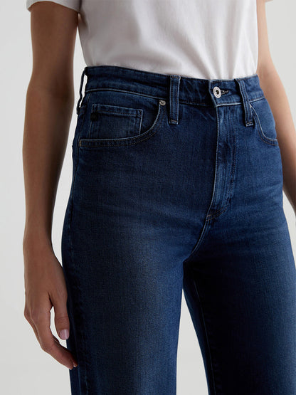 A person wearing AG Jeans Kora High-Rise Wide Leg in Midnight Sun, paired with a white shirt, stands with their hands at their sides.