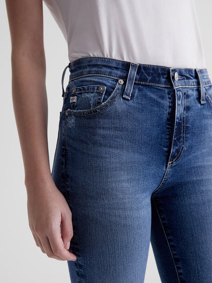 Close-up of a person wearing blue AG Jeans Mari High Rise Straight in 13 Years Disclosure denim jeans with a white top.