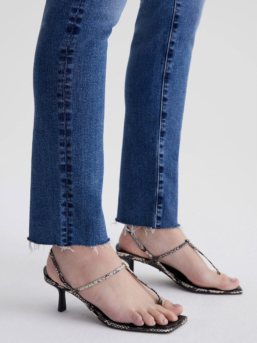 A person wearing AG Jeans Mari High Rise Straight in 13 Years Disclosure and strappy high-heeled sandals.