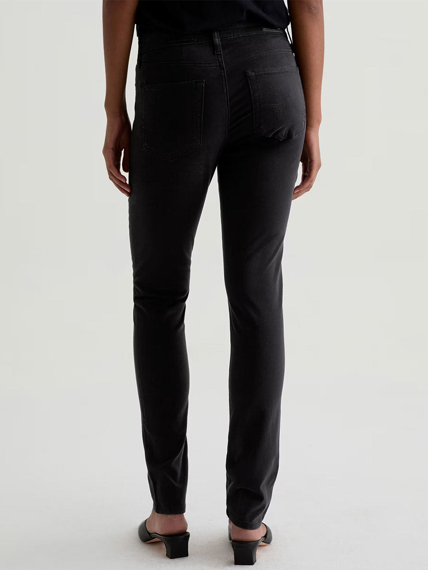 Model wears the AG Jeans Prima Cigarette Leg in Super Black with black open-toe shoes, shown from the back against a plain light background.