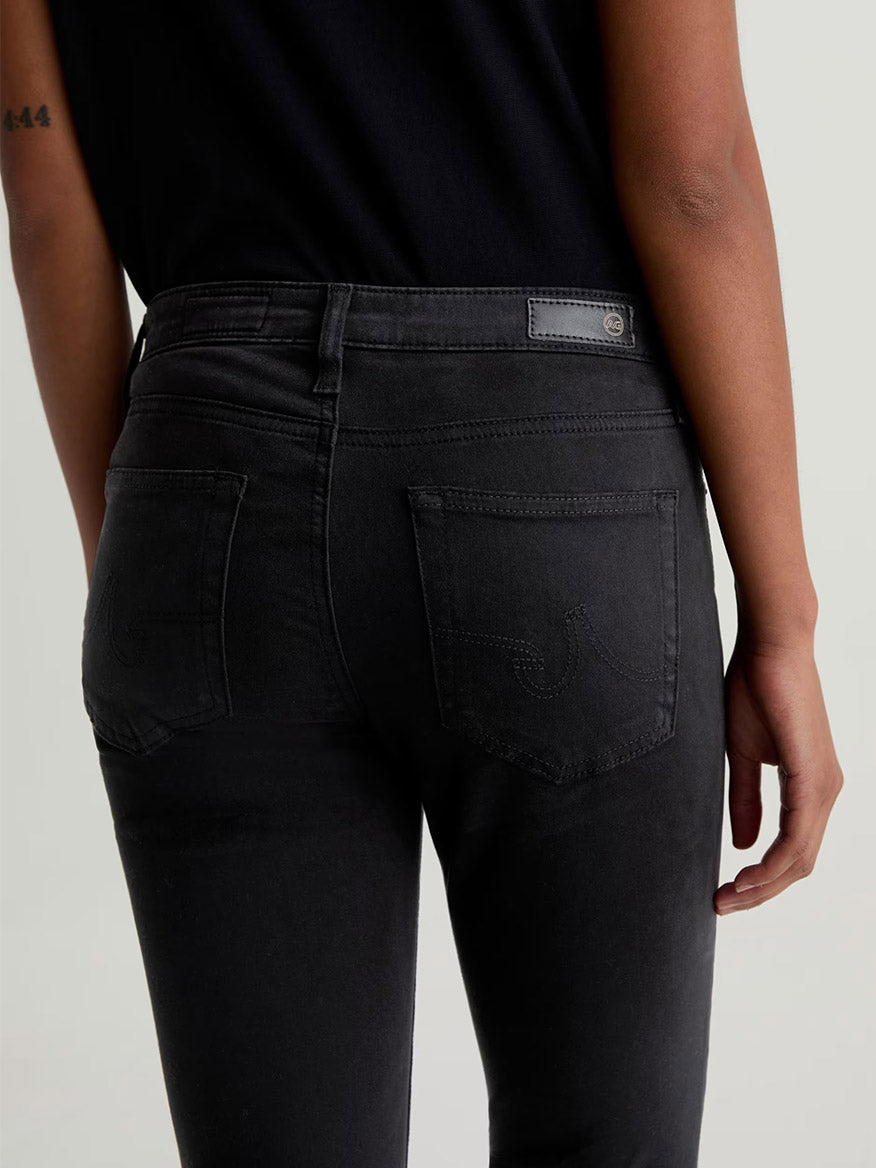 Person wearing AG Jeans Prima Cigarette Leg in Super Black and a black top, shown from the back with one arm resting by their side.
