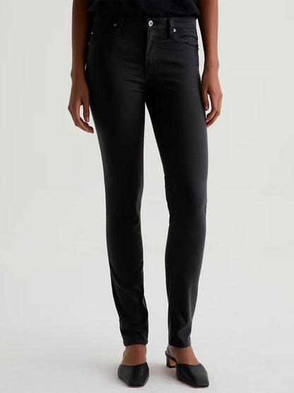 Model wears AG Jeans Prima Cigarette Leg in Super Black with black pointed flats, standing against a plain light background. Only the lower half of the body is visible.