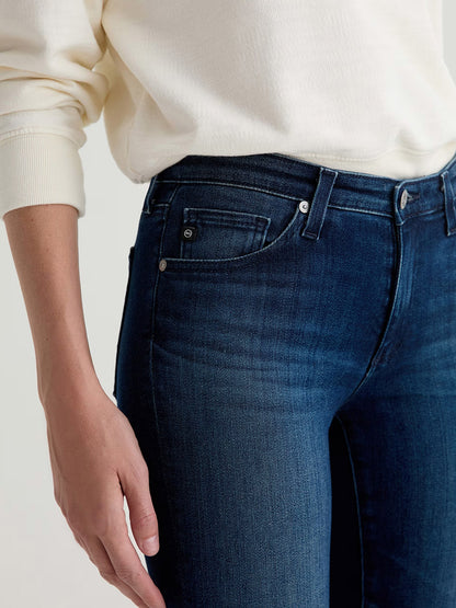 A person wearing a cream long-sleeve shirt and AG Jeans Prima Cigarette Leg in Epilogue, shown from mid-torso to upper thighs, with one hand relaxed at their side.