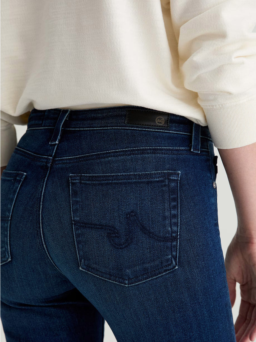 Model wears AG Jeans Prima Cigarette Leg in Epilogue—a dark blue, comfort-stretch denim style—paired with a light-colored sweater; shown from the back at waist level.