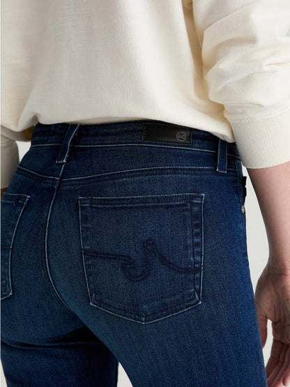 Model wears AG Jeans Prima Cigarette Leg in Epilogue—a dark blue, comfort-stretch denim style—paired with a light-colored sweater; shown from the back at waist level.