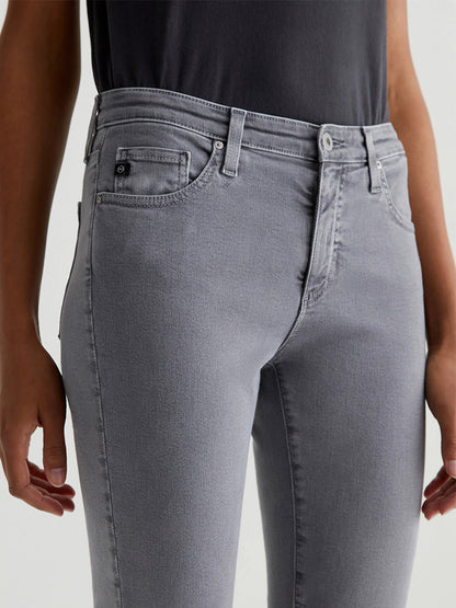 Person wearing AG Jeans Prima Cigarette Leg in Sulfur Grey Ember and a black top, standing with arms at their sides.