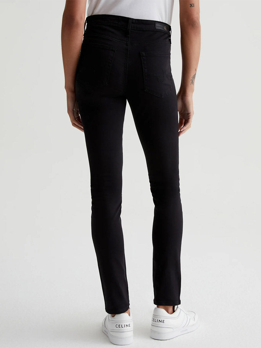 The back view of a woman wearing AG Jeans Prima Cigarette Leg in Super Black jeans with a super stretch wear.