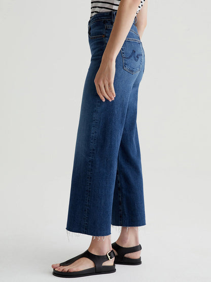 Person wearing AG Jeans Saige Wide Leg Crop in Plume with a frayed hem, paired with a striped top and black sandals.