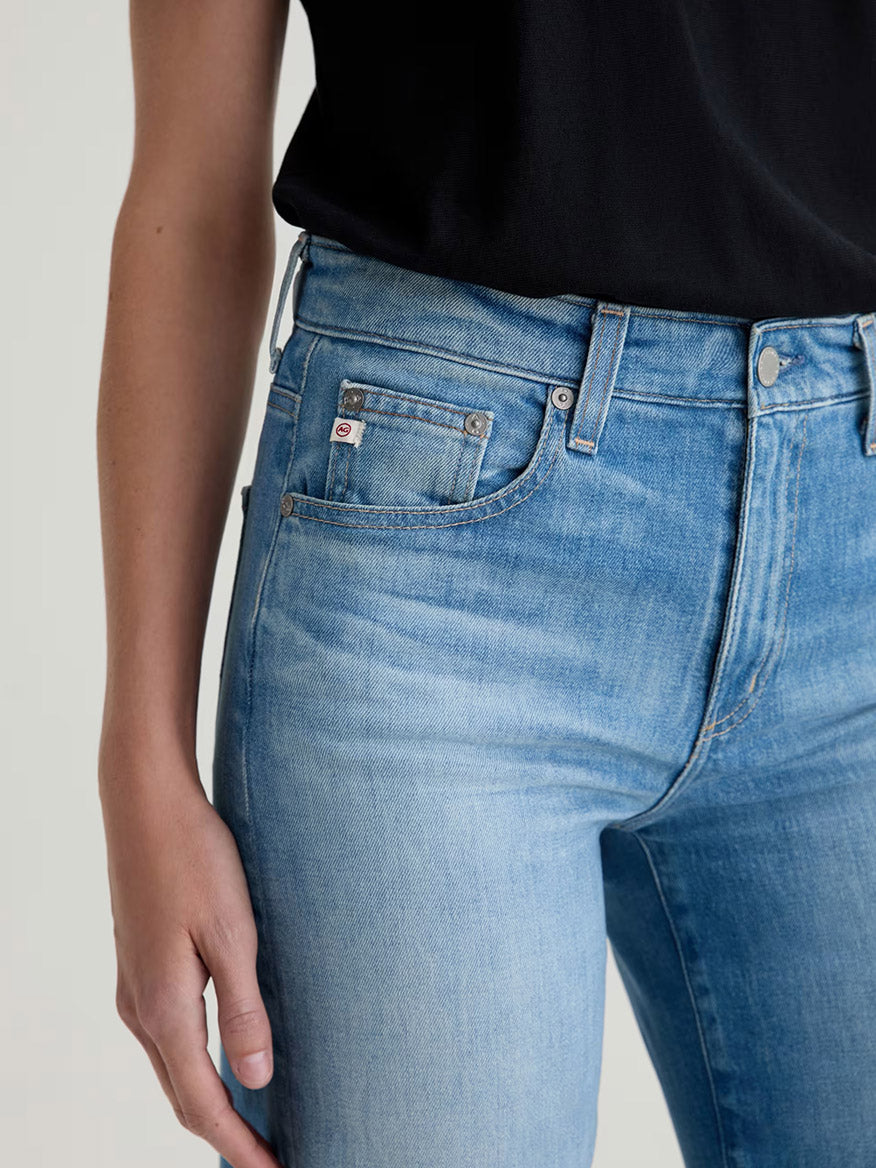 A person wears a black top and AG Jeans Saige Wide Leg Mid-Rise in 18 Years Bisou, shown from mid-torso to mid-thigh.