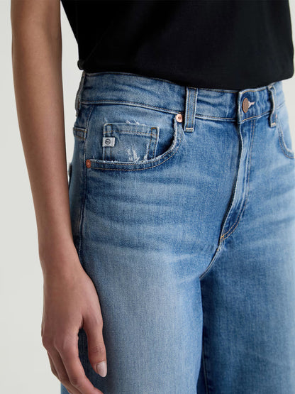 A person wearing a black top and AG Jeans Saige Wide Leg Mid-Rise in American West, shown from waist to mid-thigh.