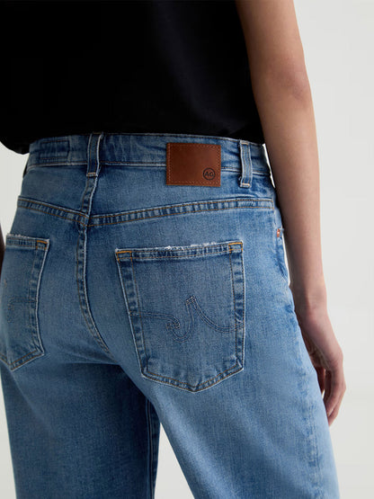 Model wearing AG Jeans Saige Wide Leg Mid-Rise in American West—light blue stretch denim jeans with a brown leather patch on the waistband, visible back pockets, and paired with a black top; shown from the back.