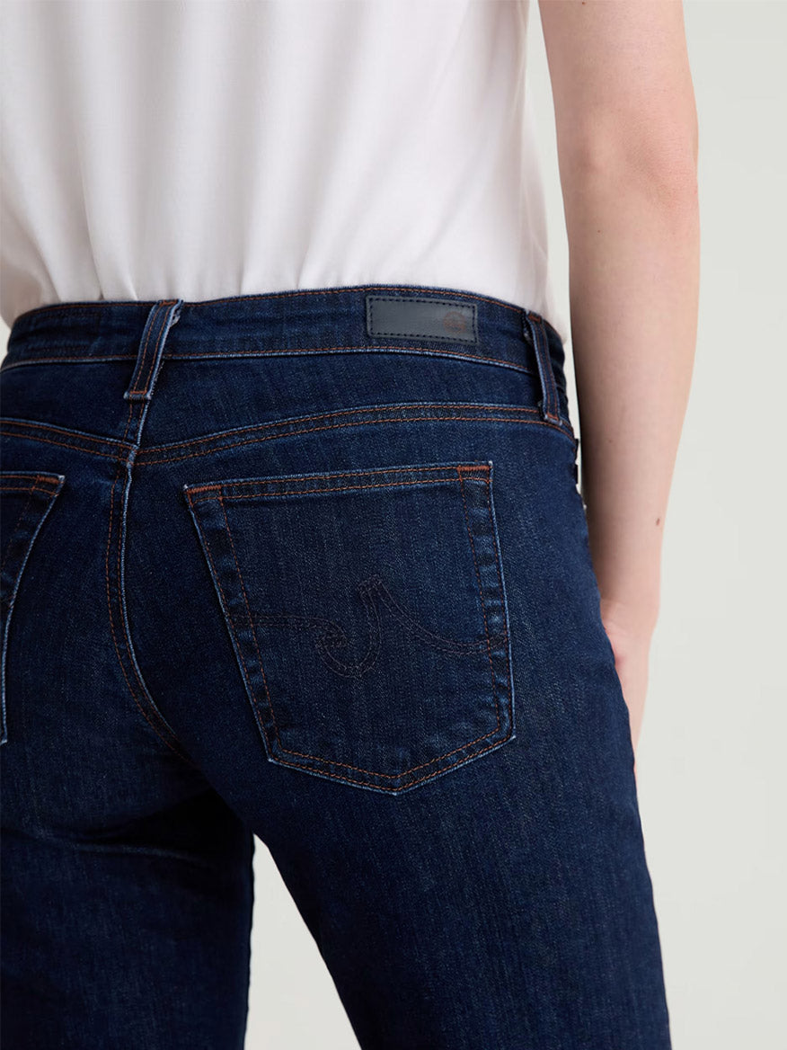 A person wearing AG Jeans Sandra Low-Rise Straight in Modern Indigo and a white top, photographed from the waist down and viewed from behind.